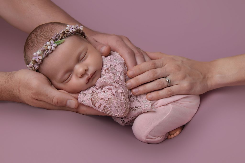 Newborn girl in pink outfit with parents hands
