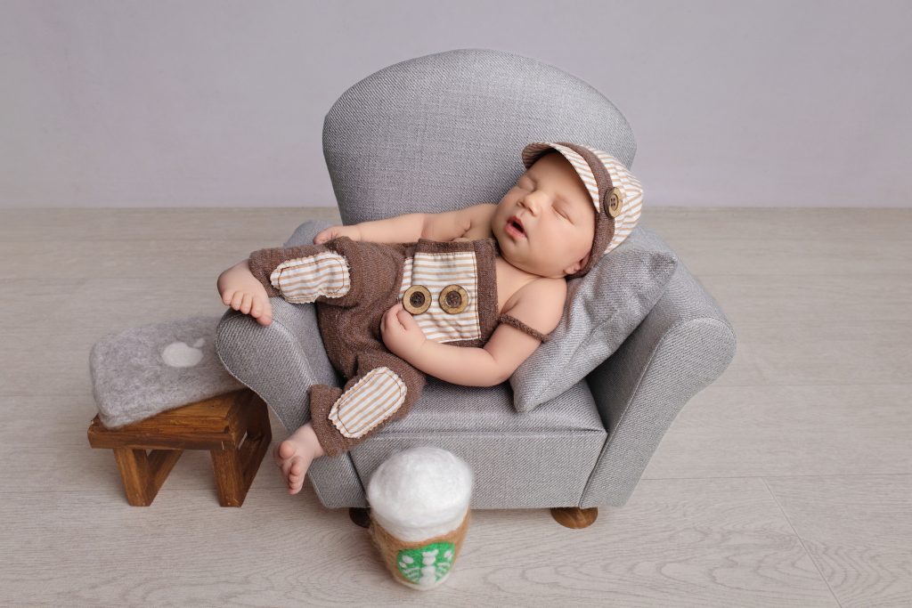 Newborn boy in brown outfit posed on a tiny couch